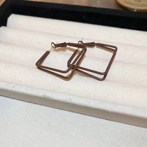 Detailed view of dark brown geometric square hoop earrings on a beige velvet display tray