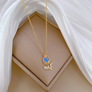 Close-up of gold tulip pendant featuring iridescent gem and zircon leaves on white silk