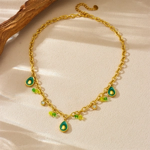 Collier doré avec pendentif avocat vert et perles de cristal sur fond beige texturé