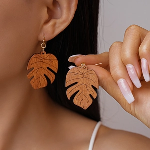 Detail of wooden monstera leaf earrings with golden hooks worn by a model