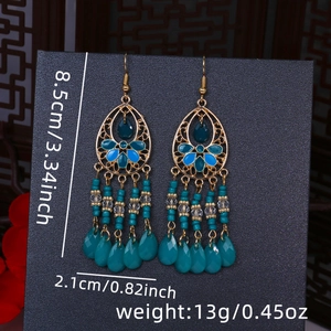 Dettaglio macro di orecchini boho con motivi floreali blu e frange di perline chic