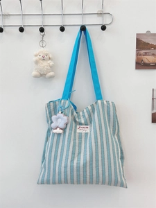 Dettaglio della borsa tote in tela a righe blu con ciondolo a fiore su parete bianca