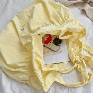 Detail of light yellow pleated canvas tote bag with adjustable knotted shoulder strap bow