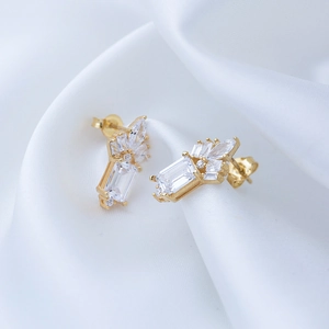 Macro shot of rectangular gold earrings with clear zircons on white silk background