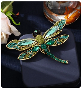 Macro detail of gold dragonfly brooch with green crystals on a jewelry box