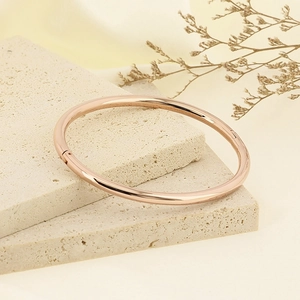 Detail shot of a rose gold minimalist oval bangle on a textured stone display pedestal