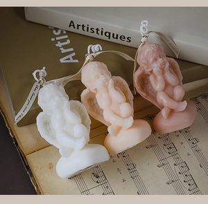 Trois bougies parfumées en forme d'ange blanc et rose sur une partition vintage