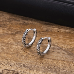 Macro shot of vintage silver earrings with floral embossed texture on wooden background