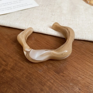 Detailed shot of irregular wave acrylic cuff featuring coffee marble texture on wood