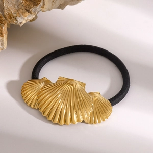 Detail view of black elastic hair band with three golden shell charms on stone background