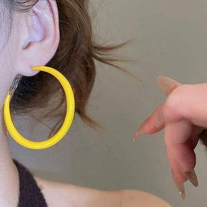 Gros plan sur une grande boucle d'oreille créole en émail jaune brillant