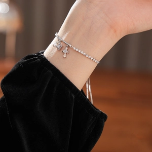Close-up of zircon cross diamond and pearl bracelet worn on wrist with black velvet sleeve