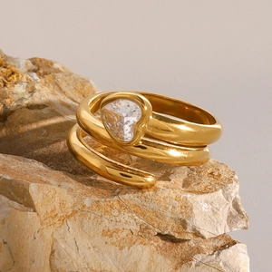 Macro detail of a gold spiral heart ring with clear zircon on a natural stone base