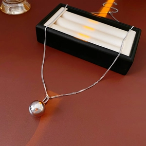 Detail of silver titanium steel ball necklace on a brown leather surface with a black box