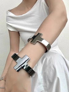 Polished silver metal cross open cuff bracelet shown on a model against a white wall
