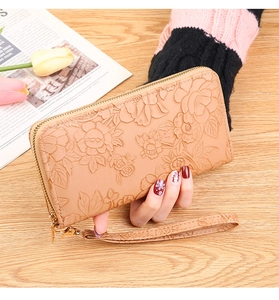 Detailed view of khaki embossed floral wallet held by a model in a cozy setting
