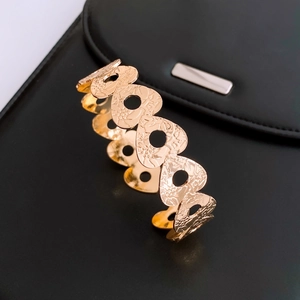Detail of golden heart-shaped hollow bangle with floral texture on black leather
