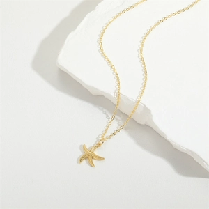 Gold plated starfish pendant necklace on a textured white stone surface in a minimalist style