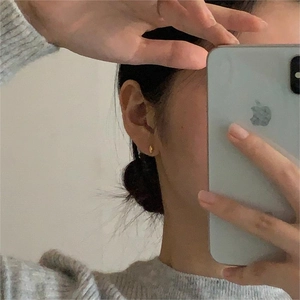 Minimalist gold ball stud earrings worn by a model in a casual lifestyle indoor setting