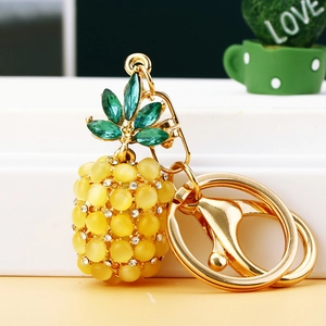 Golden pineapple keychain with yellow opal stone and green crystal leaves on white surface