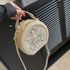 Close-up of vintage floral embroidery and golden zippers on a beige round bag