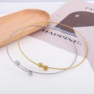 Minimalist gold and silver open choker necklaces displayed on a wooden tray with a magazine