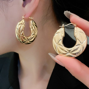 Detail of gold-plated hoop earrings featuring intricate geometric diamond cut texture