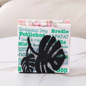 Nordic black metal napkin holder with monstera leaf design on white marble surface