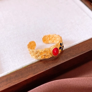 Close-up of vintage gold ring with red oval stone and blue floral decorative details