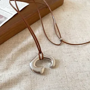 Minimalist metallic irregular C-shape pendant necklace with brown cord on linen fabric