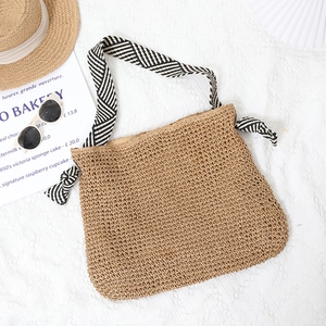 Minimalist straw woven shoulder bag with striped strap on white fabric background