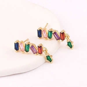 Macro shot of gold earrings with multicolored rectangular zircons on a white stand