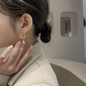Close-up of a model wearing golden metal hoop earrings with elegant beaded texture