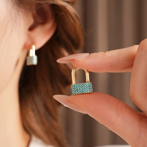 Close-up of gold lock earring with turquoise beads shown on ear and held by hand