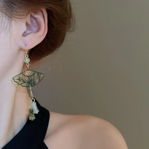 Detail of green fan-shaped tassel earrings with bamboo pattern on a model