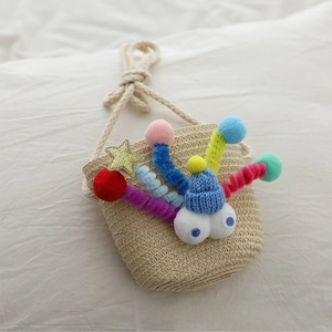 Close-up of handmade straw bag featuring colorful pompoms and cartoon eye decorations