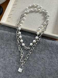 Detail of layered silver link chain and pearl necklace with rectangular padlock pendant