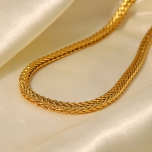 Primo piano della collana intrecciata placcata oro su un elegante tessuto di seta beige
