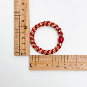 Detailed view of red and gold woven hair tie with red oval bead and 5cm diameter