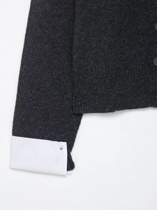 Detail of charcoal grey knit cardigan featuring layered white shirt cuffs and buttons