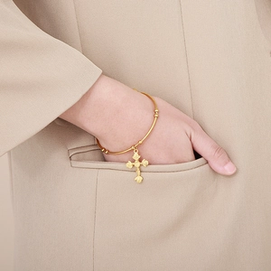 Detail of a thin gold cross bangle with rose motifs worn by a model in a beige blazer