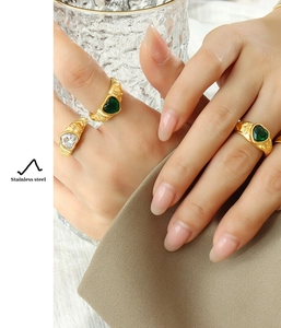 Macro detail of wave-textured gold rings with heart-shaped green and clear crystals