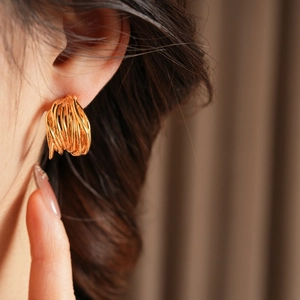 Detailed view of layered gold-plated C-shape earrings on model with elegant winding texture