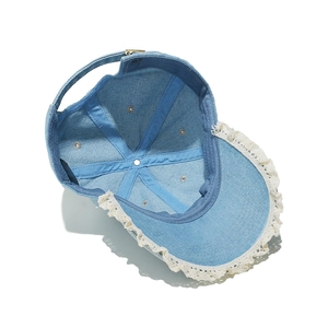 Détail de la casquette en jean bleu clair avec dentelle blanche et boucle métallique
