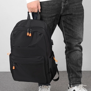 Detail of black nylon backpack featuring a USB charging port and orange zipper pulls
