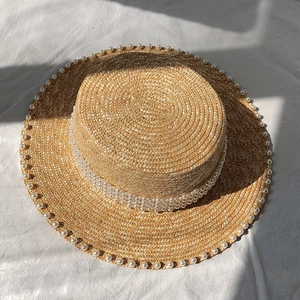 Detail of straw hat with pearl chain trim and flat top under bright sunlight