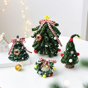 Handmade green DIY Christmas trees and wreath with red bows and bells on a cozy desk
