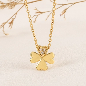 Golden clover necklace with heart-shaped leaves and zircon inlay on a beige textured background