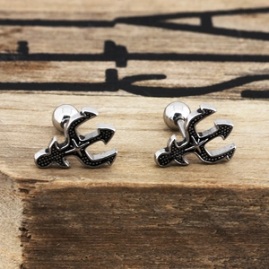 Macro detail of retro trident stud earrings in vintage silver finish on wood background