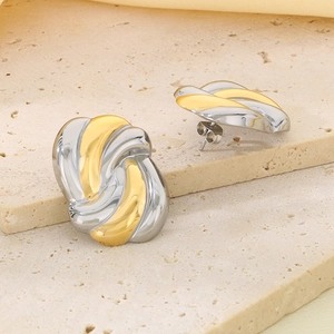 Detailed macro view of two-tone gold and silver knotted earrings on a beige stone base